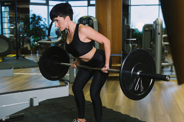 Fototapeta na wymiar Fit young woman lifting barbells looking focused, working out in a gym, doing barbell row