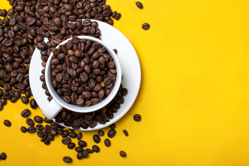Coffee cup with beans on yellow background. Top view with copy space