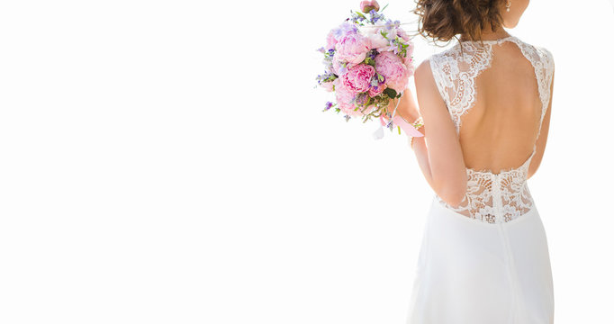 Beautiful bride on a white background. On the bride is a long wedding dress with lace and an open back. Bouquet in hands.