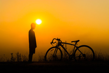 Obraz premium a person standing next to a bicycle, silhouetted against a bright orange sunset.
