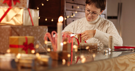 Woman in thick white cable sweater wrapping presents on the background of Christmas decorations and lights