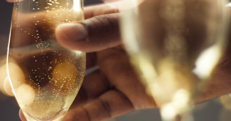 Close up of a man's hand picking up a flute glass with sparkling wine with bubbles in gray and gold tones
