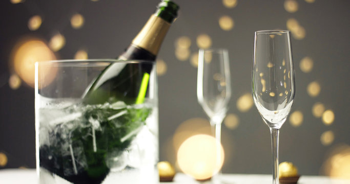 Bottle of sparkling wine with three flute glasses with bubbles floating up on gray backgrounds with Christmas lights