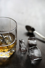 Whiskey in a glass and pieces of ice on a wood