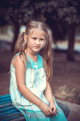 Fototapeta premium Portrait of a little girl in the park on a bench