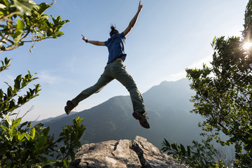 young woman jumping on cliff's edge with raised hands to the sunrise