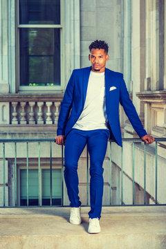 African American college student studying in New York, wearing blue suit, white T shirt, sneakers, sitting on railing in vintage office building on campus, taking break. Instagram filtered effect..
