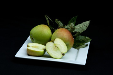 Apples on a white plate with a black background. One of the apples has been sliced open to show the inside.
