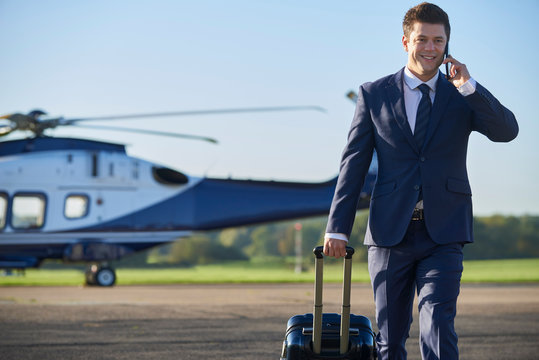Businessman Walking Away From Helicopter Whilst Talking On Mobile Phone