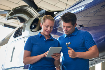 Aero Engineer And Apprentice Working On Helicopter In Hangar Looking At Digital Tablet