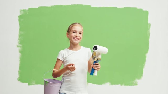 Cheerful child turns around at camera. Girl standing front green wall and holds paint roller