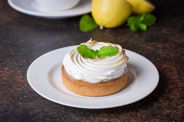 Delicious Lemon tart tartlet with merengue and cup of tea with lemon on dark stone concrete table background. Copy space