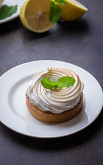 Delicious Lemon tart tartlet with meringue and cup of tea with lemon on dark stone concrete table background. Copy space