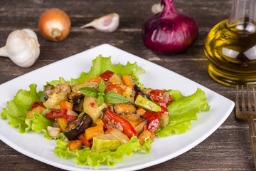 Stewed vegetables in a white bowl on wooden table. Close up