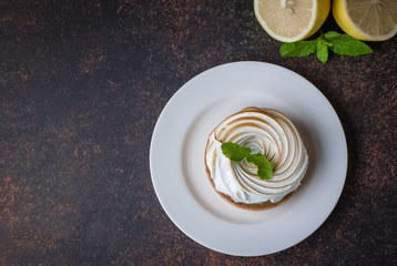 Delicious Lemon tart tartlet with meringue and cup of tea with lemon on dark stone concrete table background. Copy space