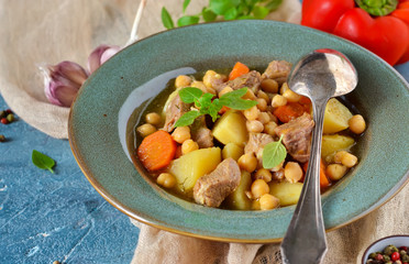 Homemade stew with potatoes, carrots and chickpeas on a blue background.