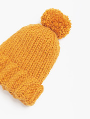 Mustard knit beanie hat with big pom pom isolated on white background. Copy space. Flat lay. Top view