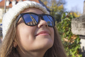 Sights of the old city are reflected in the glasses on the face of a young smiling girl, close-up, Munich, Germany