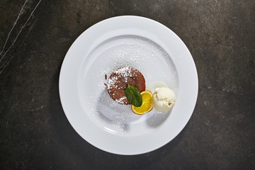 Chocolate fondant with ice cream, slice of orange and mint leaves on black background