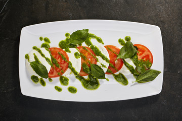 Caprese with tomatoes and mozzarella with pesto sauce on  black background