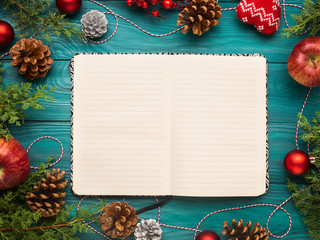 Open notebook on christmas background with pine cones and ornaments. Festive flat lay with white pages