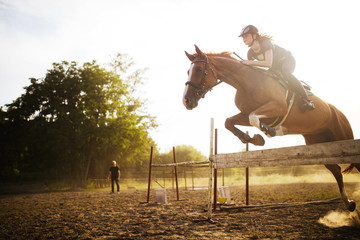 Young female jockey on horse leaping over hurdle