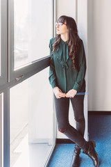 Young business woman looking standing near window looking outside - thinking, worried, inspiration concept