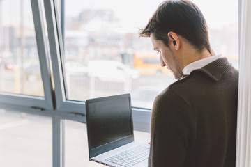 Young handsome caucasian businessman standing near window using computer hand hold - technology, business, connected concept