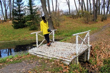 A woman in a yellow coat is standing on a birch bridge in the estate of Count Leo Tolstoy in Yasnaya Polyana.