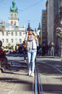 Casual stylish girl wears hat and eyeglasses walking in old city street, autumn sunny day