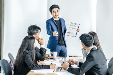 Photo of successful young manager standing making a presentation financial diagram while the others listening to him