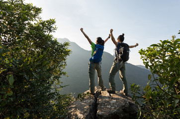 two young women successful backpackers enjoy the view on cliff's edge