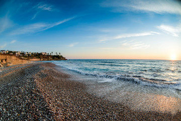 View of the beautiful sunset over the sea with wild pebble beach coast. Fisheye effect