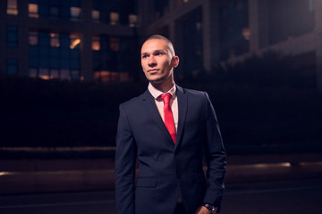 One young adult man, businessman, suit, formal wear, outdoors, night evening dark portrait modern building exterior