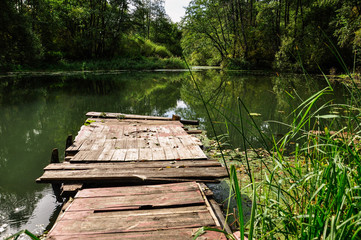 Pier on a calm river in the summer. Wooden pier bridge in the morning. Place for fishing in the river.