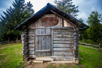 Old small wooden house on top of a hill in the forest against a dramatic sky background. Small old wooden guest house. Travel and hiking