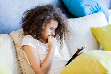 Teen girl resting and usiing digital tablet on sofa at home