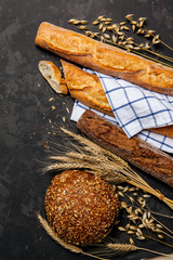 Top view of rustic bread, french baguette and wheat on dark background . Rural kitchen or bakery