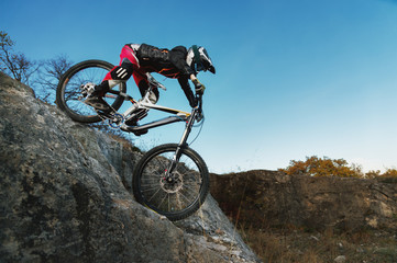 young rider on mtb bike coming down from a cliff against a blue sky