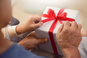 Asian boy and elderly man holding on red ribbon of white gift box.