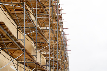 Fototapeta premium Metal scaffolding with wooden decking built around a historic building for restoration work and renovation of the facade. Construction works. Building construction.
