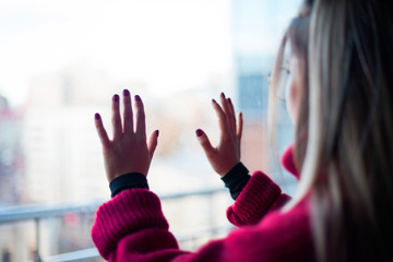 View from the back, a girl in a red sweater looks out the window at the winter city.