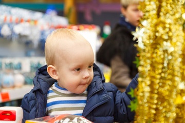 blonde babe sits in a supermarket cart and selects a Christmas tree in the store