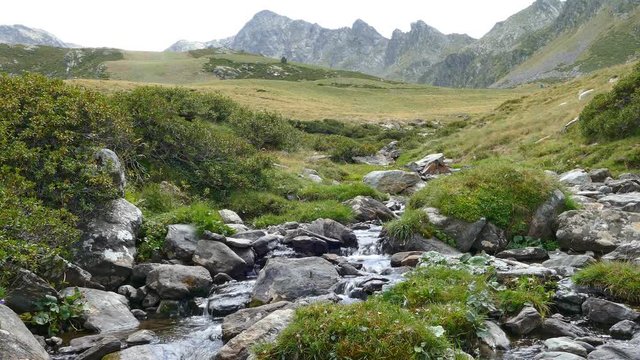 Landscape of a mountain creek, on the Pyrenees of Andorra. Little brook with the mountains in the background and with the brightness of the sky in the water.
