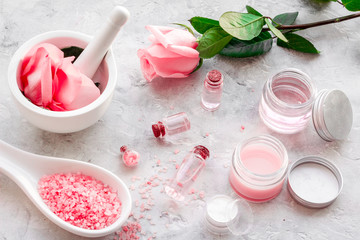 Make cosmetics with rose  oil. Mortar with rose petals and pestle on grey background