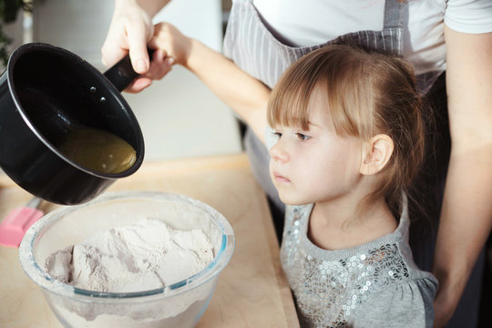 Young girl mixing ingredients for baking, pouring liquid into a bowl with flour. Lifestyle image at home kitchen, copy space.