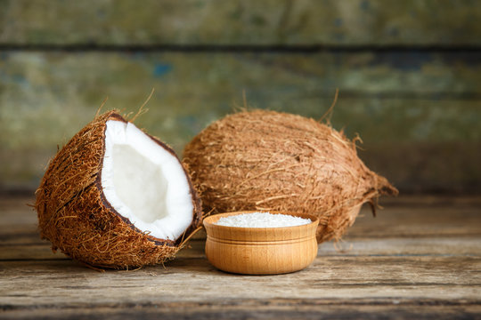 Fresh whole and cut in half coconuts with flakes on wooden background