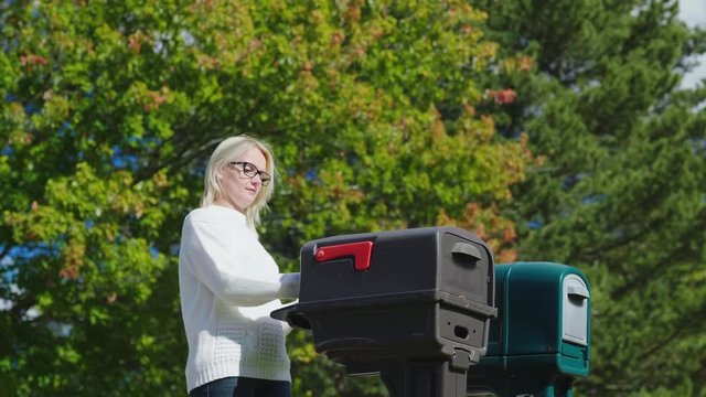 A young woman picks up mail from a outdoors mailbox