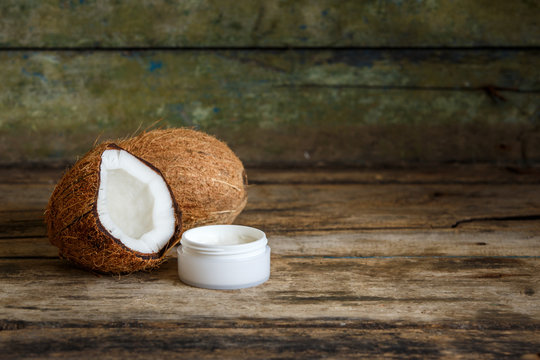 Fresh whole and cut in half coconuts with coconut cosmetics cream on wooden background with copy space
