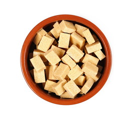 Brown cane sugar cubes in clay bowl isolated on white background, top view